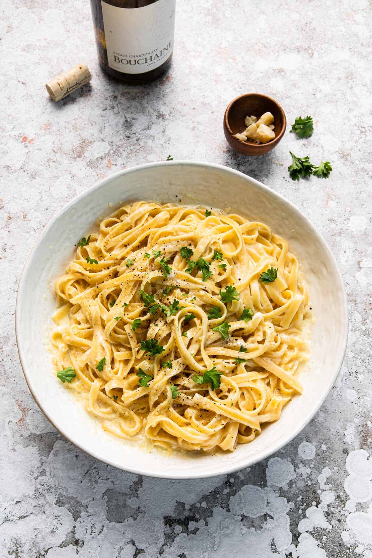 large serving bowl of fettuccine alfredo with wine bottle in background