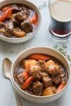 bowl of beef stew with a glass of dark beer in the background