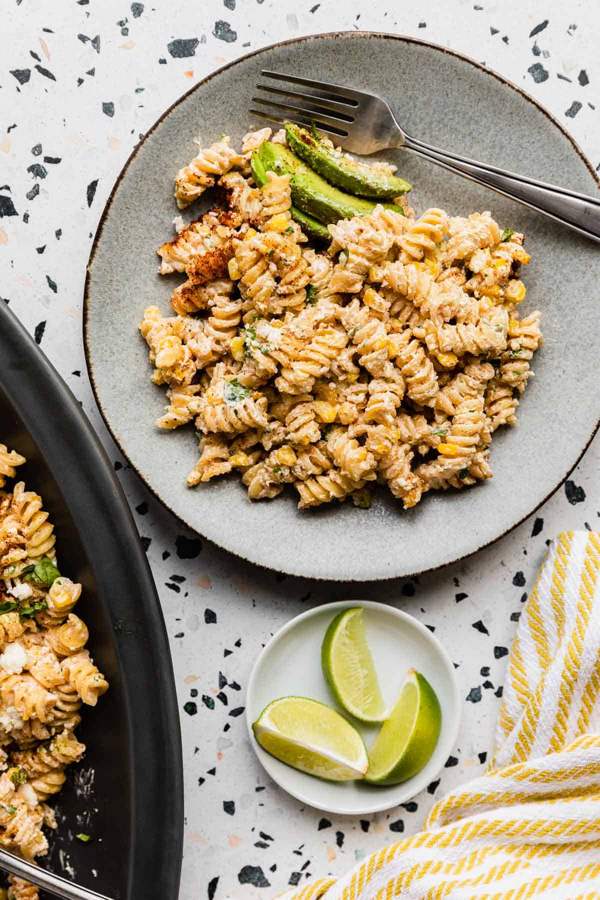 top down view with a plate of pasta salad and sliced avocado and partial view of platter on a mosaic background