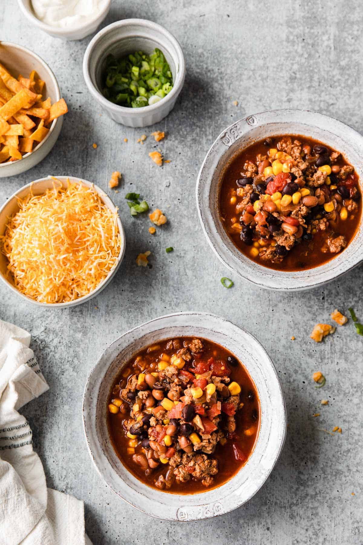 two bowls of taco soup with toppings in background