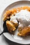 apple dump cake on a plate with melting vanilla ice cream and a spoon
