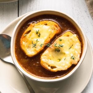 caramelized onion soup in a bowl with thyme and cheesy toasted bread