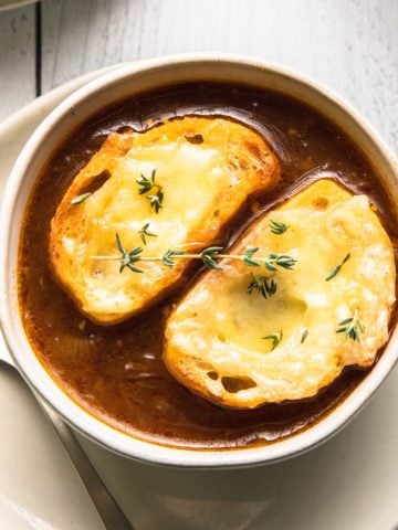 caramelized onion soup in a bowl with thyme and cheesy toasted bread