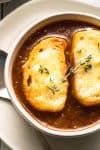french onion soup in a bowl with cheesy bread and a thyme sprig