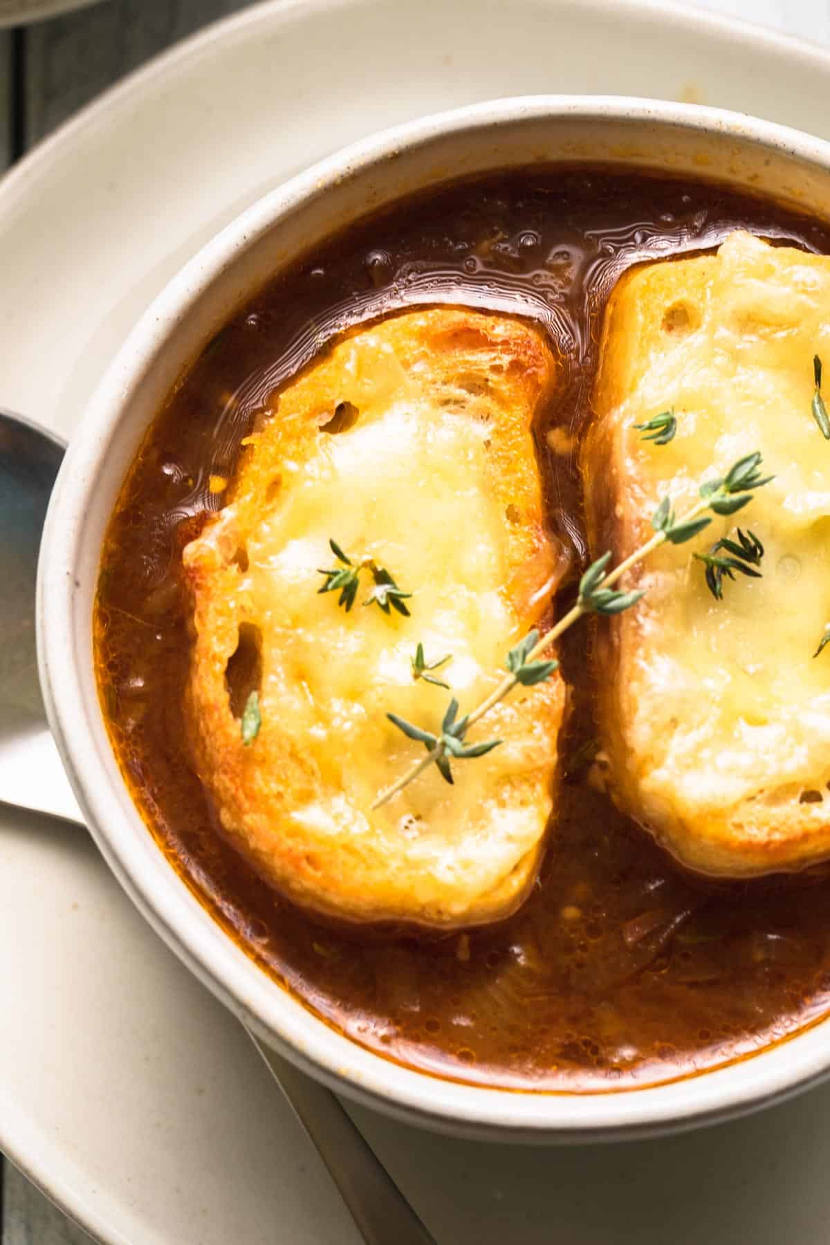 soup in a bowl with cheesy bread and a thyme sprig