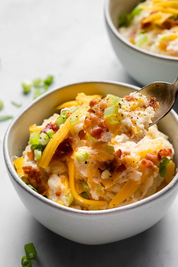 mashed potatoes in a small bowl topped with bacon, cheese, and green onions