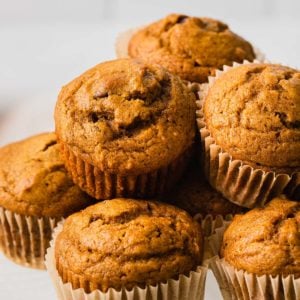 Pumpkin chocolate chip muffins stacked on a plate.