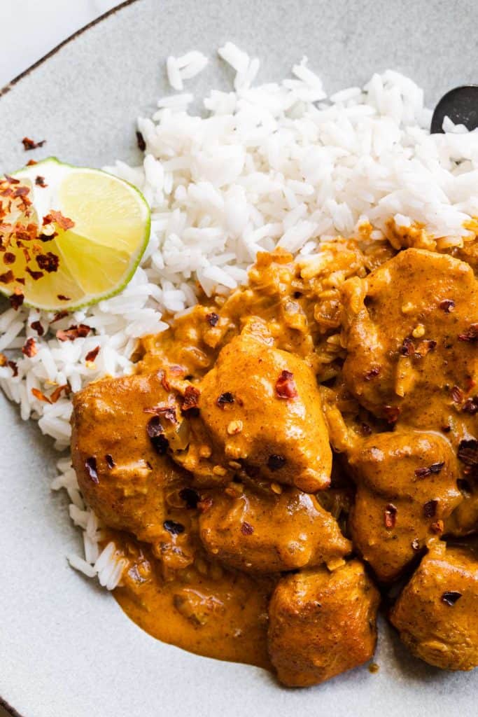 Chicken smothered in coconut curry sauce with a side of white rice and lime.