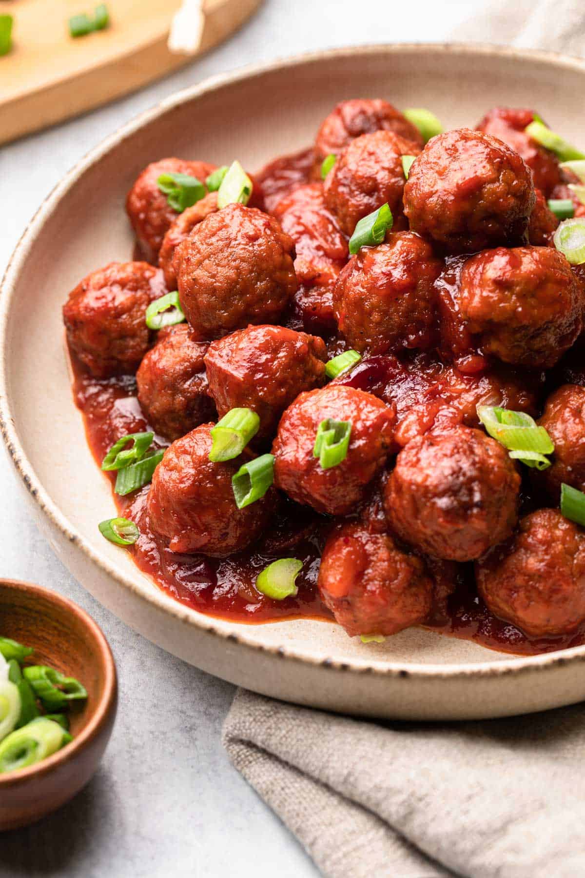 A bowl of cranberry meatballs topped with sliced green onions.