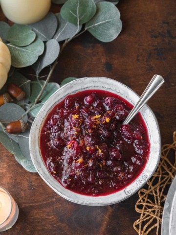A bowl of cranberry sauce on a wooden table set for thanksgiving.