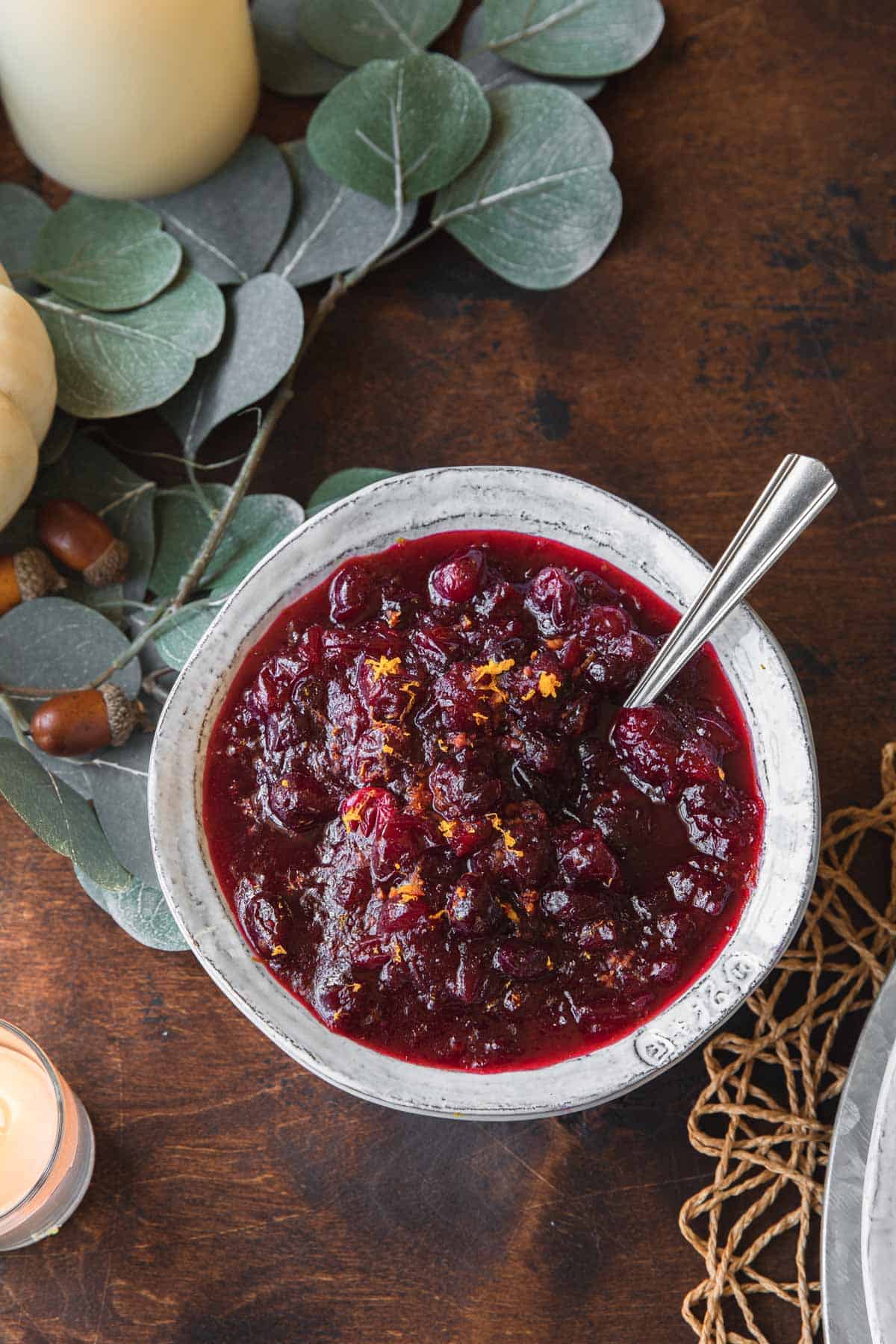 A bowl of cranberry sauce on a wooden table set for thanksgiving.
