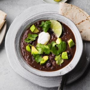 A bowl of black bean soup topped with avocado, sour cream, and cilantro.