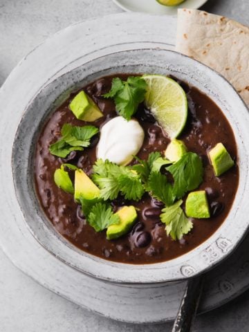 A bowl of black bean soup topped with avocado, sour cream, and cilantro.