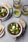 Two bowls of black bean soup topped with avocado and cilantro.