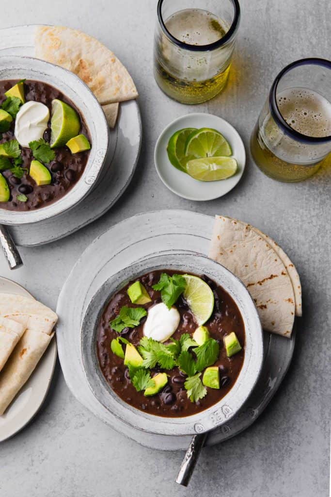 Two bowls of black bean soup topped with avocado and cilantro.