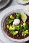 A bowl of black bean soup topped with avocado, cilantro, and sour cream.