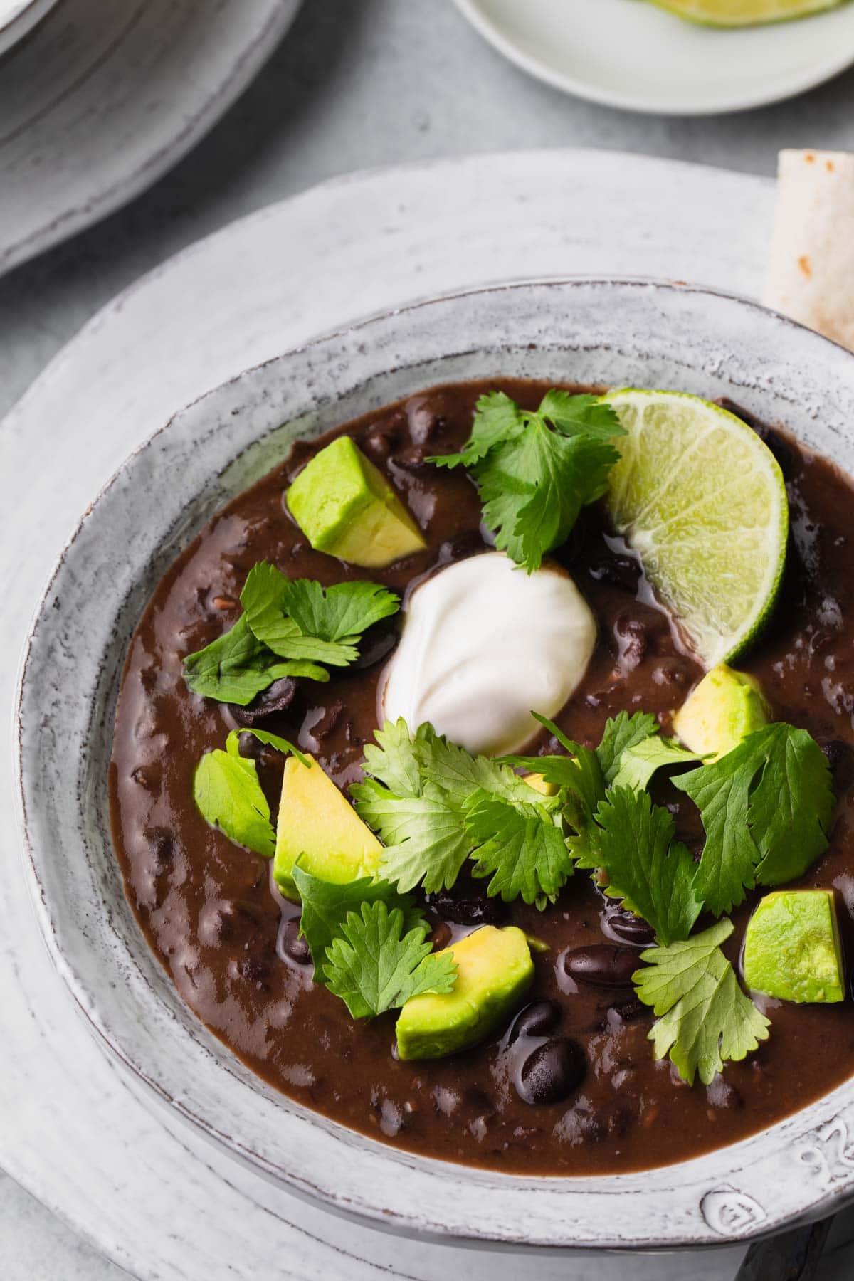 A bowl of black bean soup topped with avocado, cilantro, and sour cream.