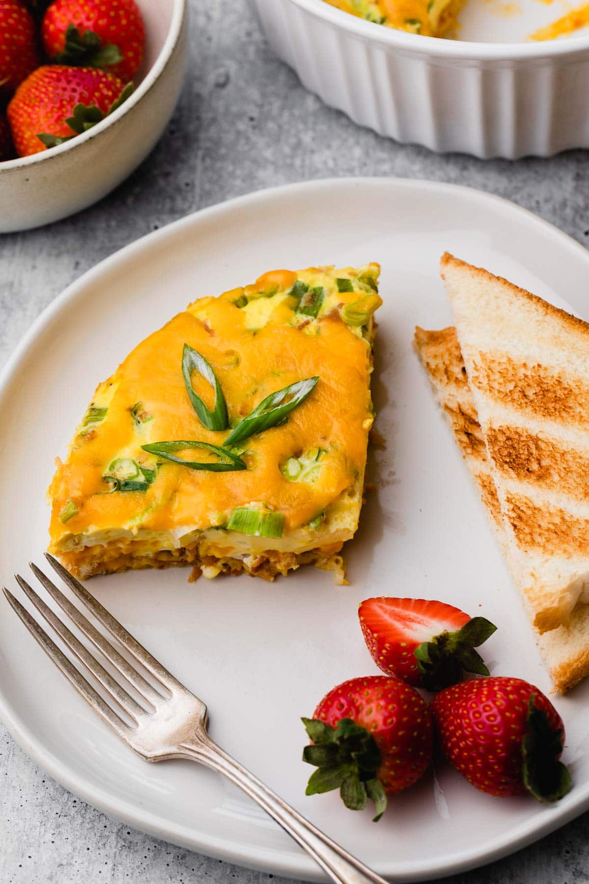 A plate of egg casserole, toast, and strawberries.