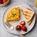 A plate of breakfast casserole, toast, and strawberries.