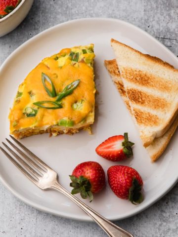 A plate of breakfast casserole, toast, and strawberries.