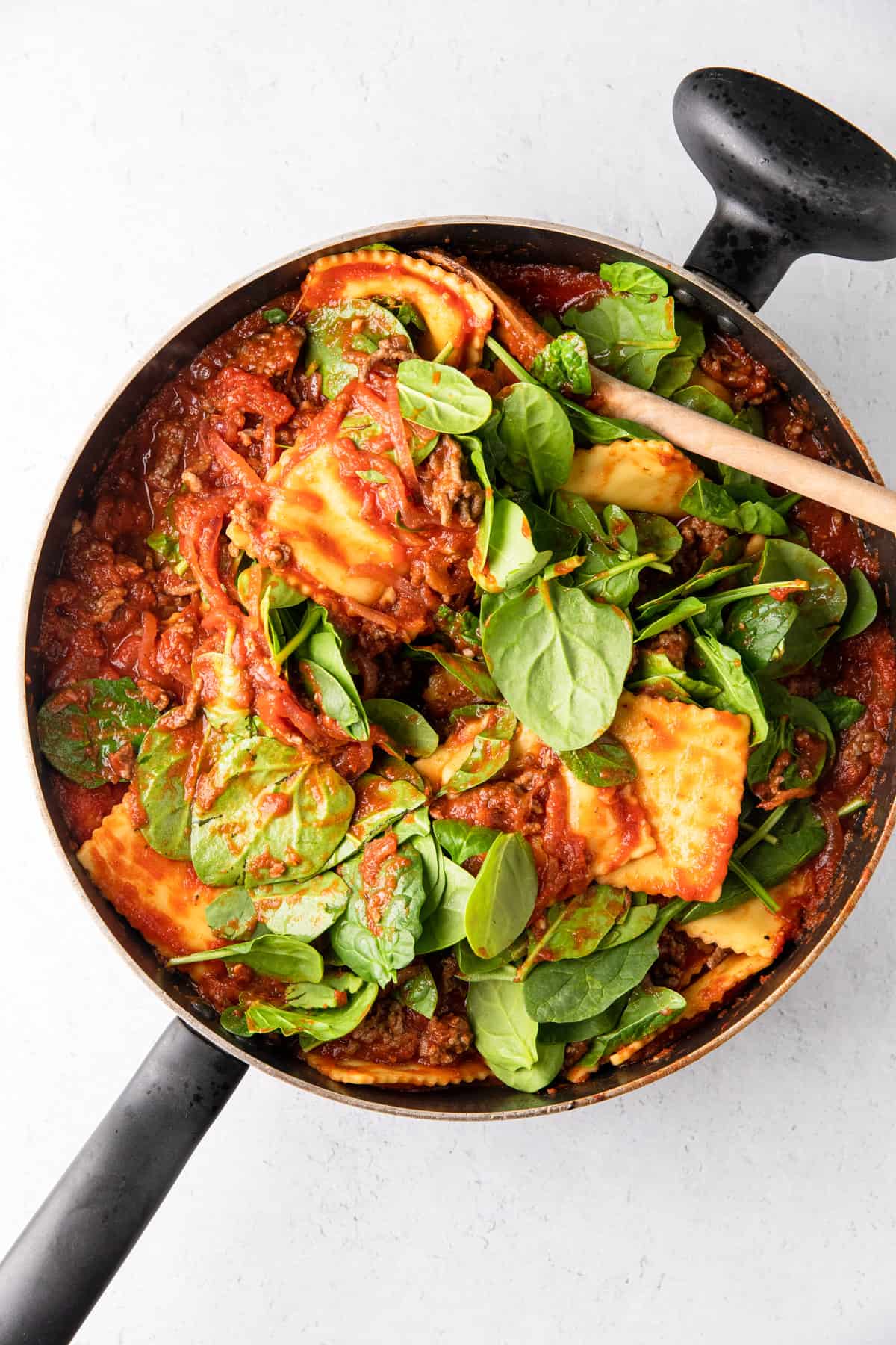 cooking ravioli in tomato sauce, adding ground beef and spinach to pan