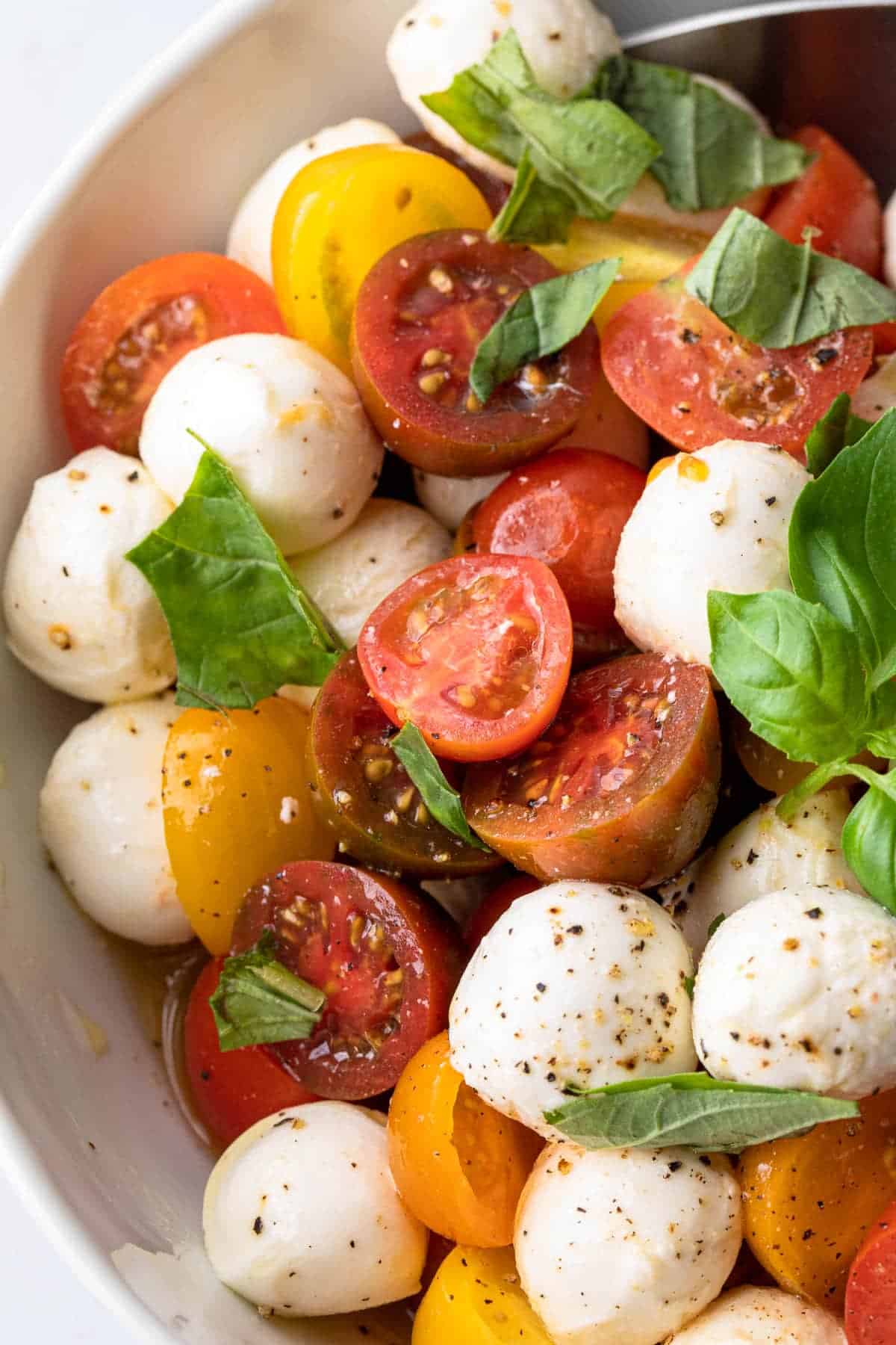 cherry tomatoes and mozzarella balls with basil leaves in a salad bowl