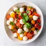 a large white bowl with a cherry tomato, mozzarella and basil salad
