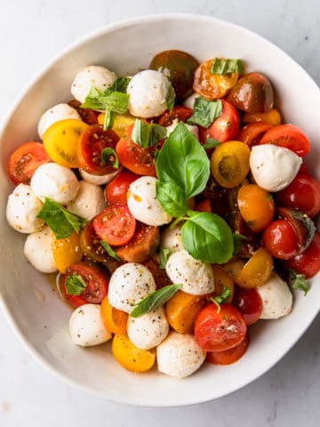 a large white bowl with a cherry tomato, mozzarella and basil salad