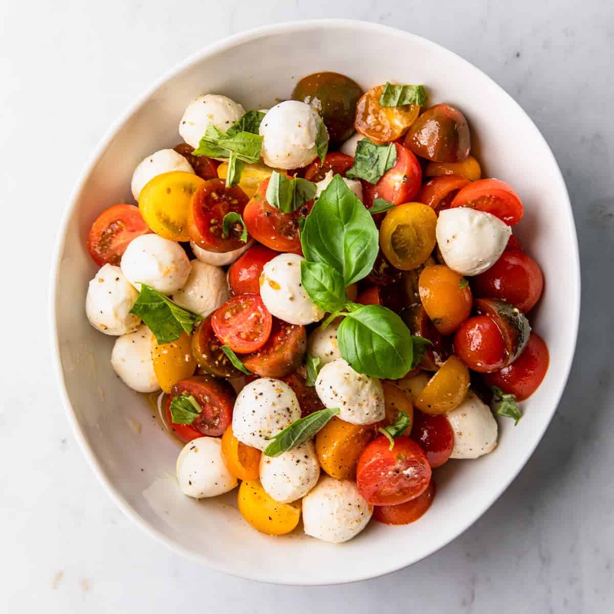 a large white bowl with a cherry tomato, mozzarella and basil salad