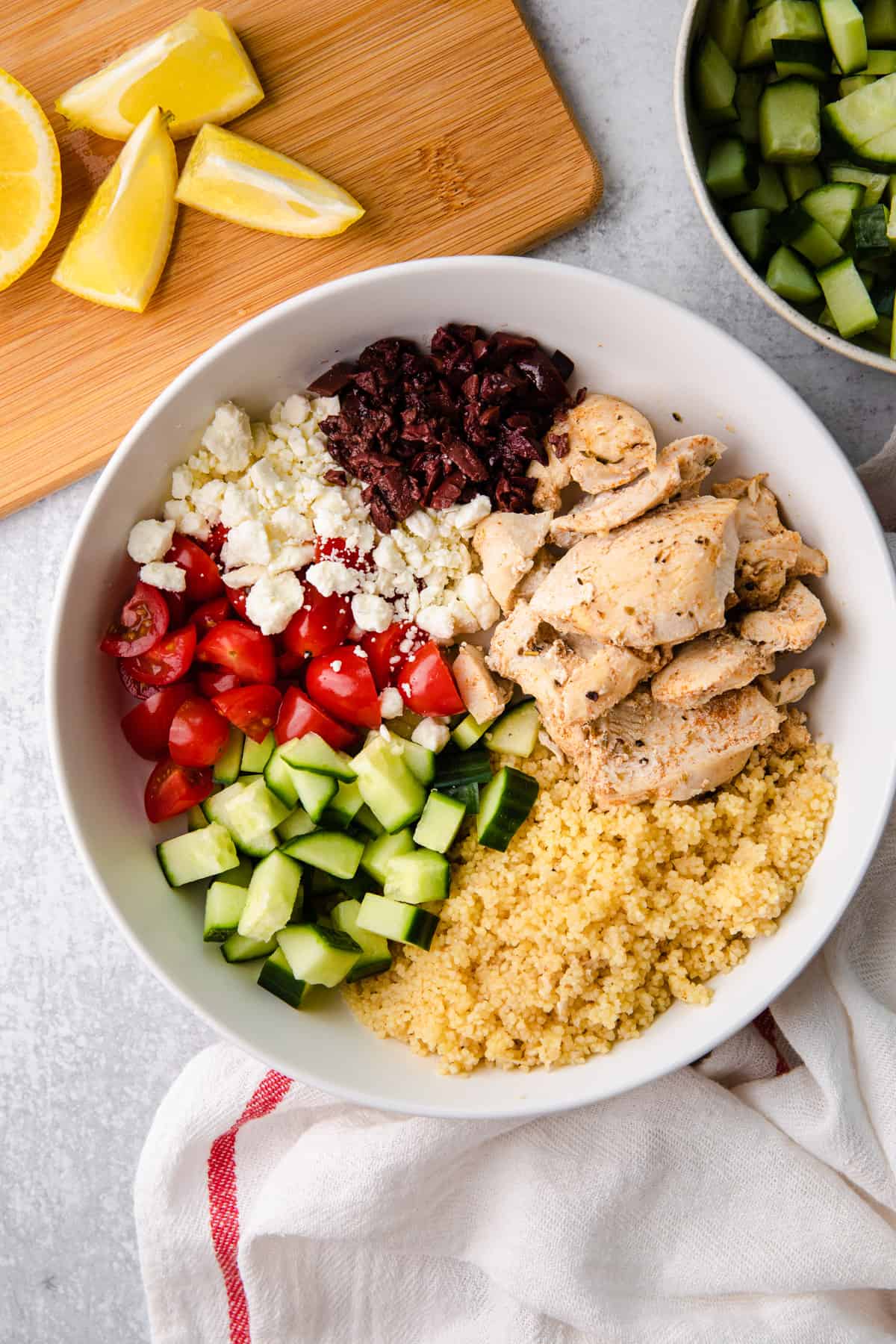 a white bowl with chicken, feta, tomatoes, cucumbers, couscous