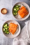 two bowls of sweet chili salmon over rice with cucumbers.