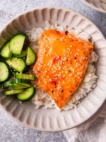 sweet chili salmon recipe prepared in a bowl over rice and cucumbers