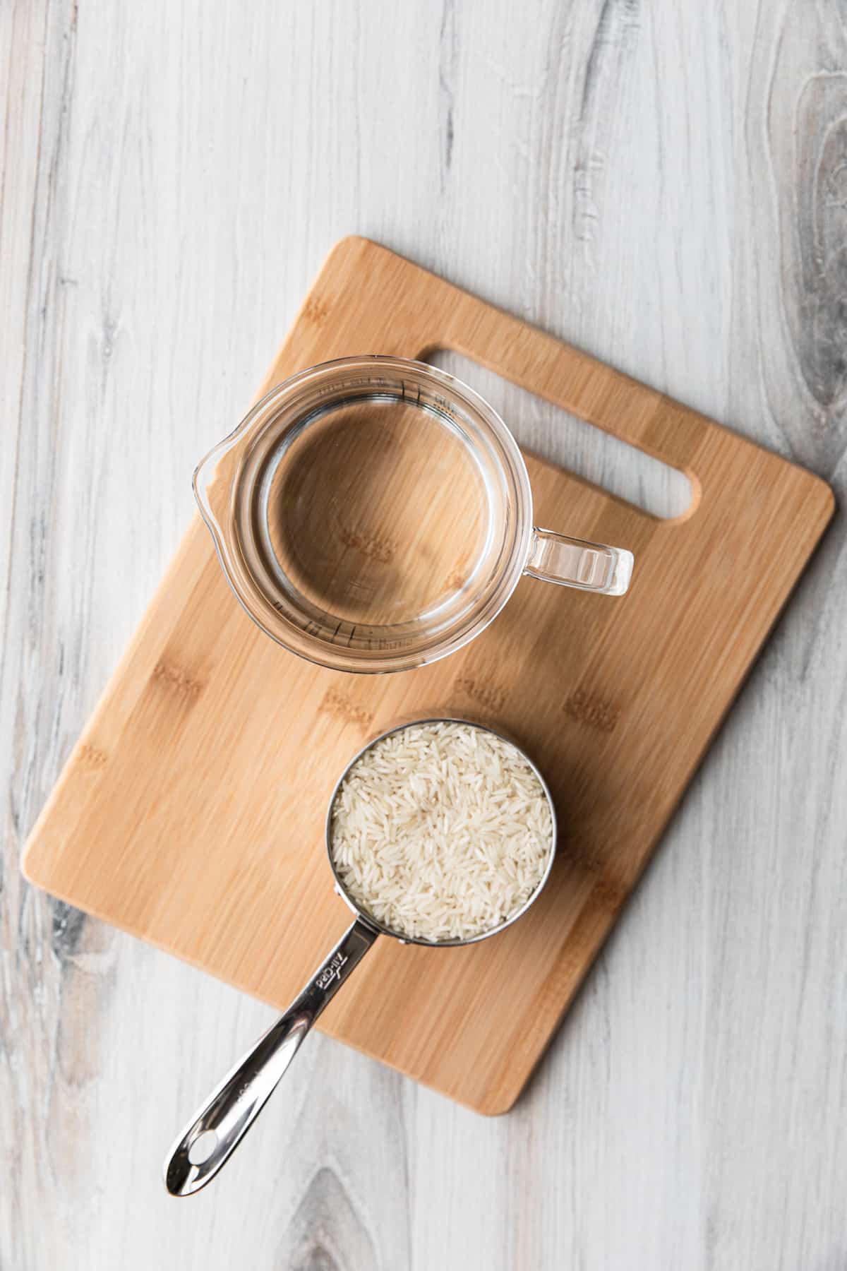 a cup of dry rice and a cup of water on a cutting board