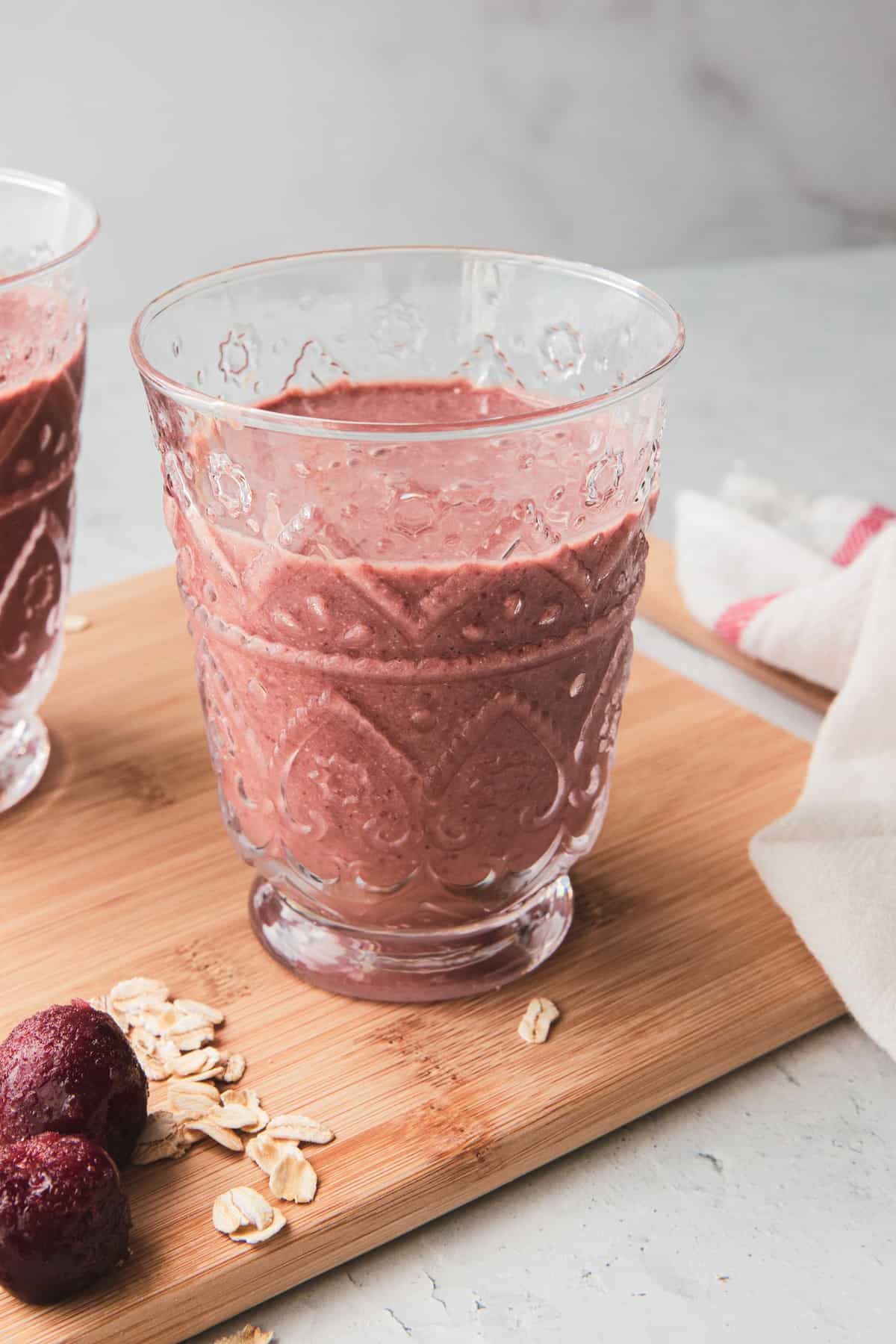 a glass of chocolate cherry smoothie on a cutting board