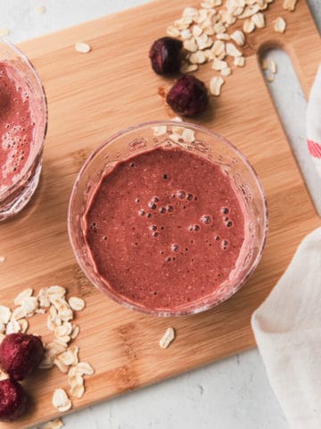 chocolate cherry smoothie on a wooden board with a few rolled oats on the side