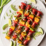 sausage kabobs on a platter with green onions and limes