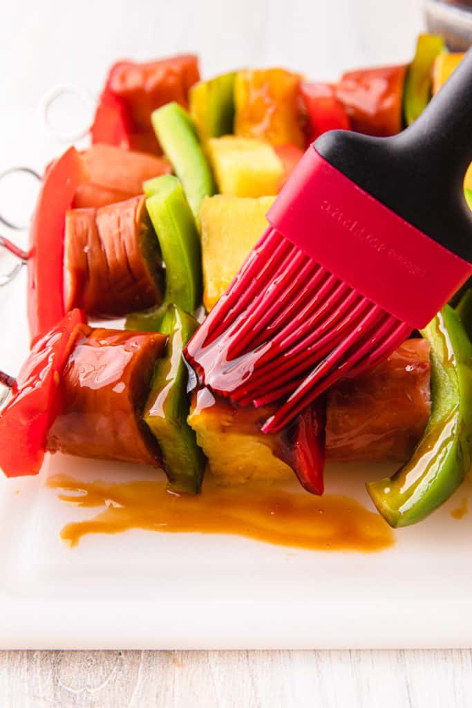 sausage and vegetables threaded on a wooden skewer while brushed with teriyaki sauce
