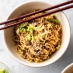 Ground beef and ramen noodles in a bowl with chopsticks and sesame seeds