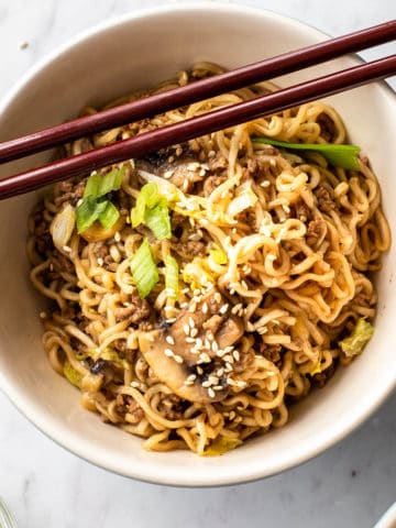 Ground beef and ramen noodles in a bowl with chopsticks and sesame seeds