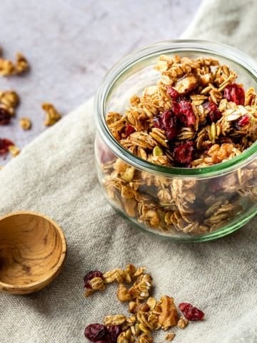 a jar of granola on a cloth with a wooden spoon on the side.