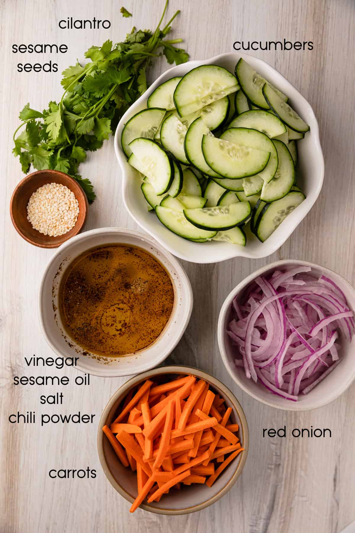 Ingredients to make the recipe: carrots, cucumbers, sesame oil, red onion, sesame seeds, cilantro, vinegar, salt, chili powder.
