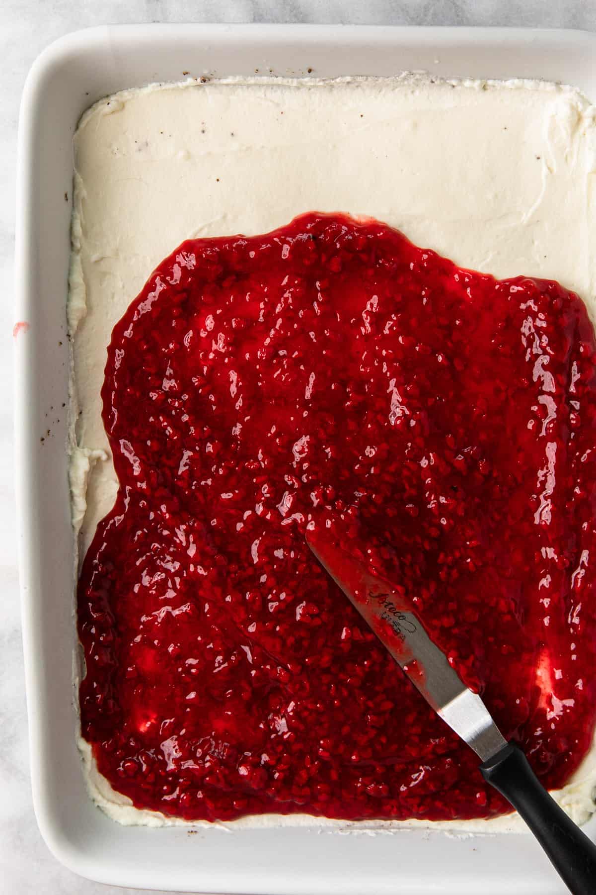 Spreading raspberry filling over cream cheese layer.