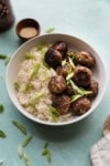 white bowl with rice and crispy meatballs garnished with green onions