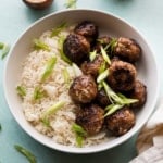 A bowl of meatballs over rice with green onion garnishes.