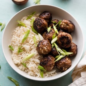 A bowl of meatballs over rice with green onion garnishes.