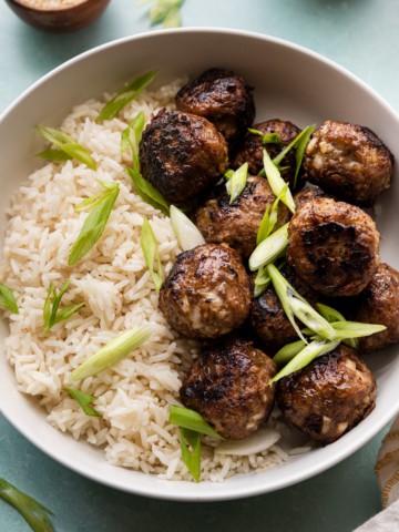 A bowl of meatballs over rice with green onion garnishes.