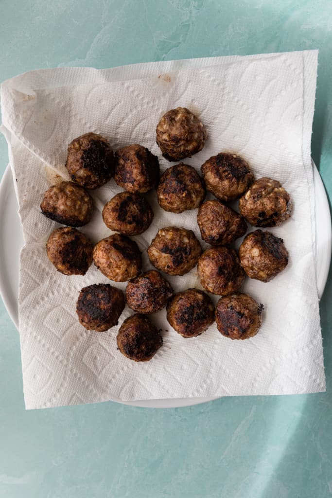 Cooked meatballs draining on paper towels.