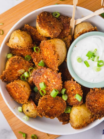 parmesan crusted potatoes in a bowl with a creamy white dip and green onions