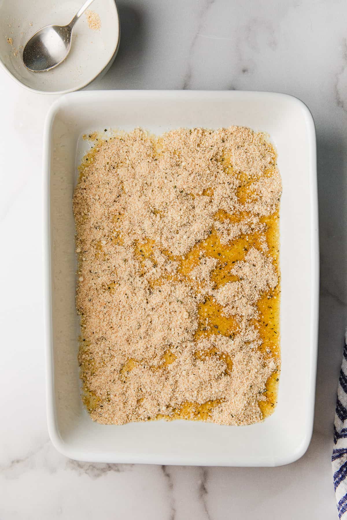 Olive oil being poured in a baking dish. Parmesan mixture in baking dish.