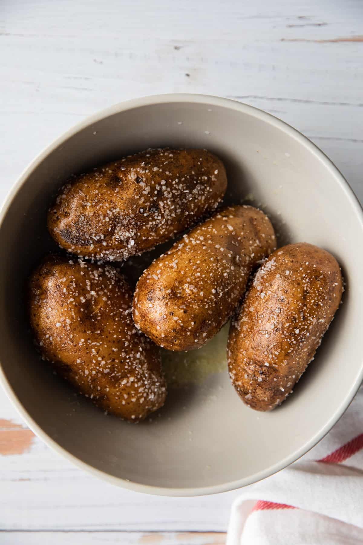 4 potatoes in a bowl that have been rubbed with oil and sprinkled with salat